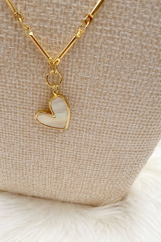 Gold necklace with a heart-shaped pendant on a textured beige surface
