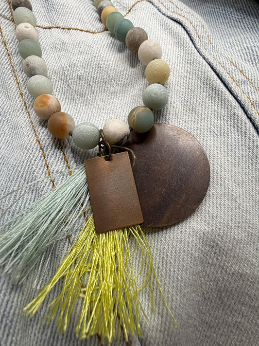 Necklace with beads, leather tag, and tassel on a textured fabric background