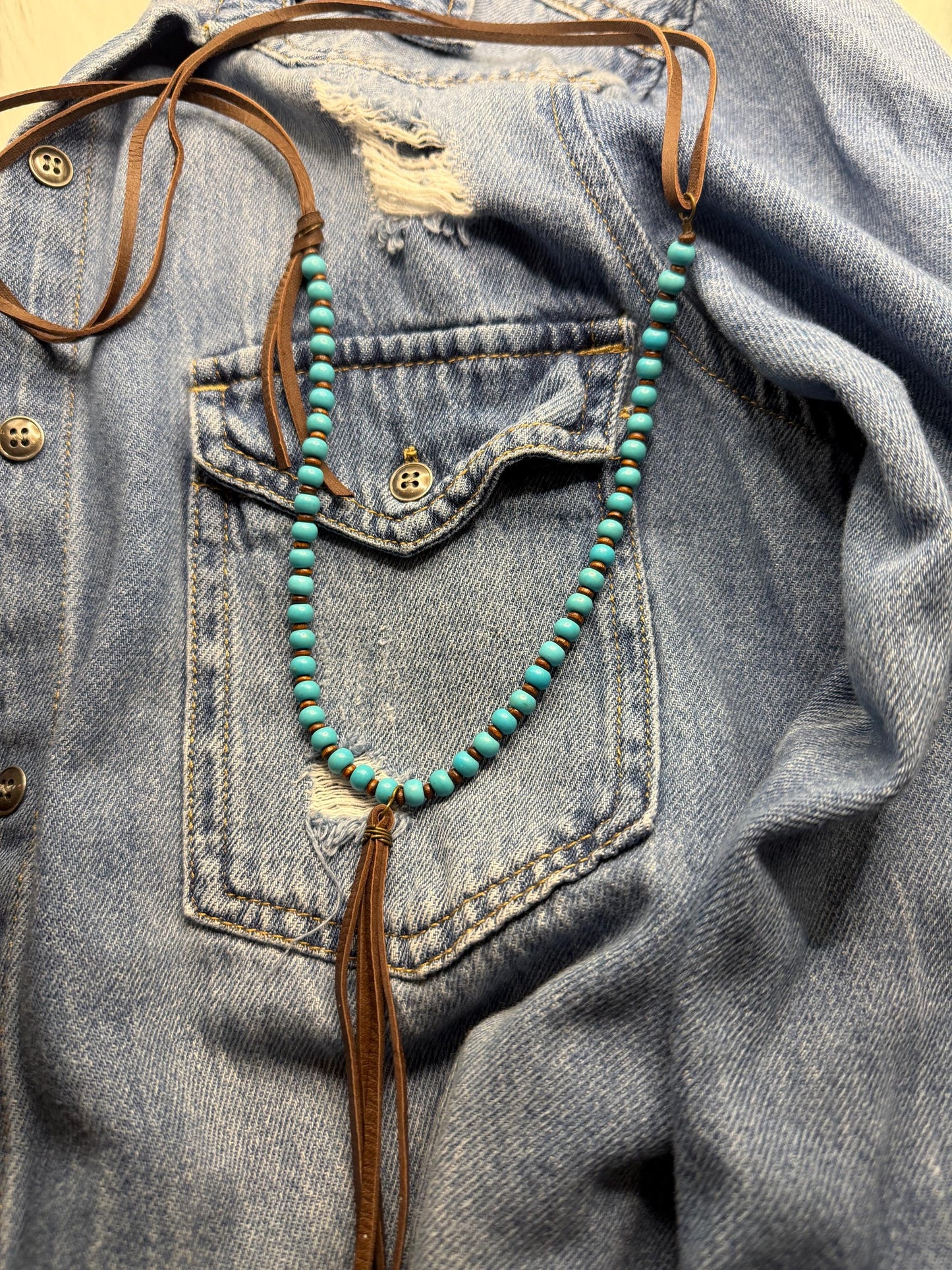 Turquoise beaded necklace with tassel hanging from a denim jacket.