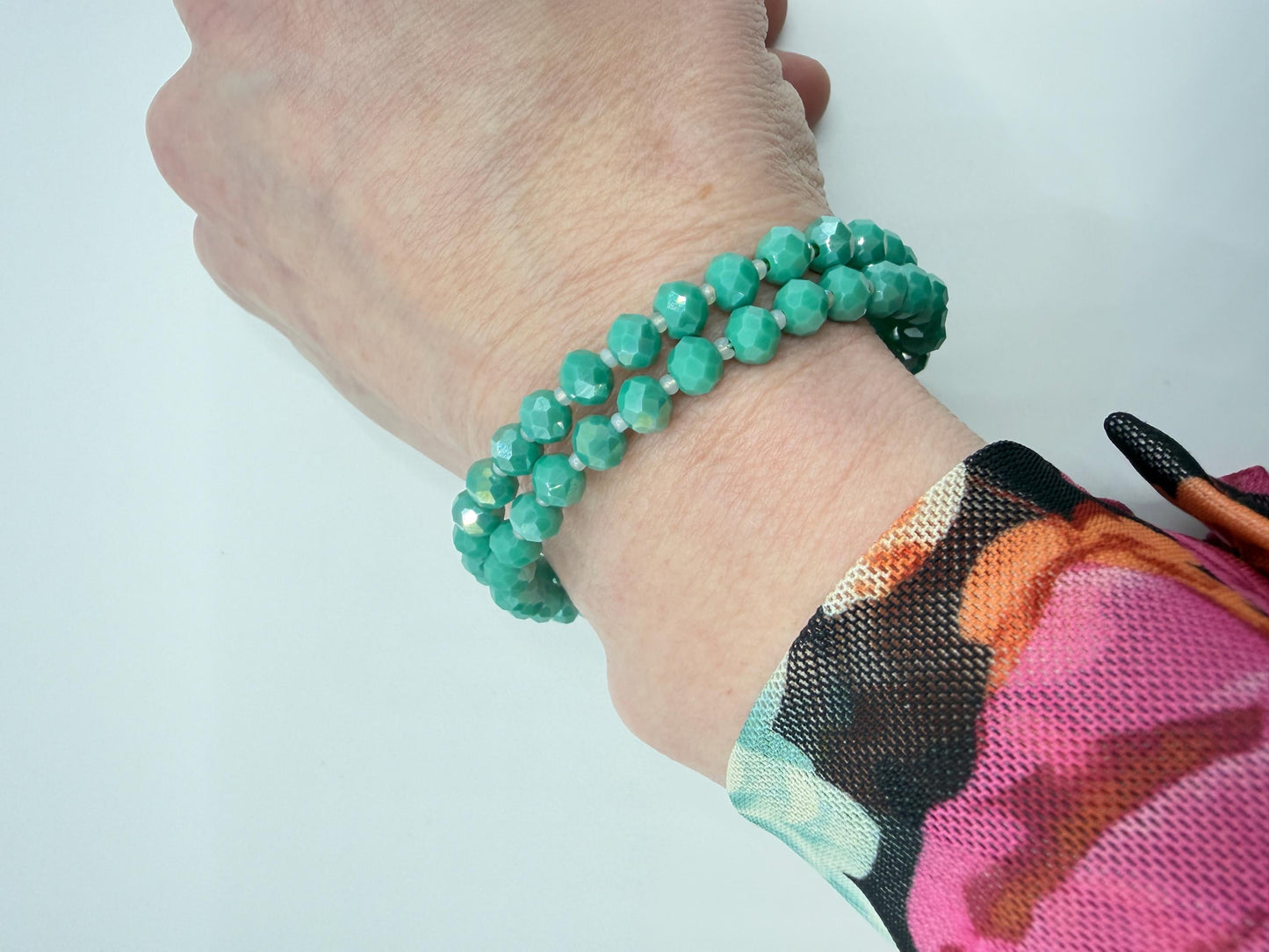 Hand wearing a green beaded bracelet on a light background