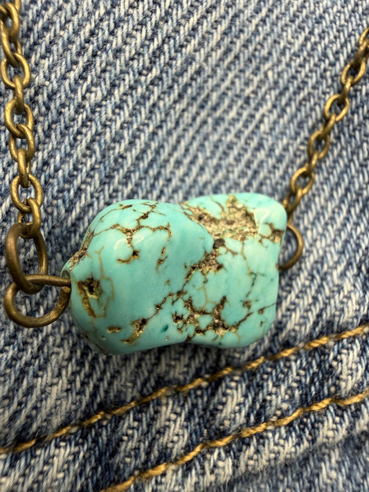 Turquoise stone necklace with gold chain on denim fabric