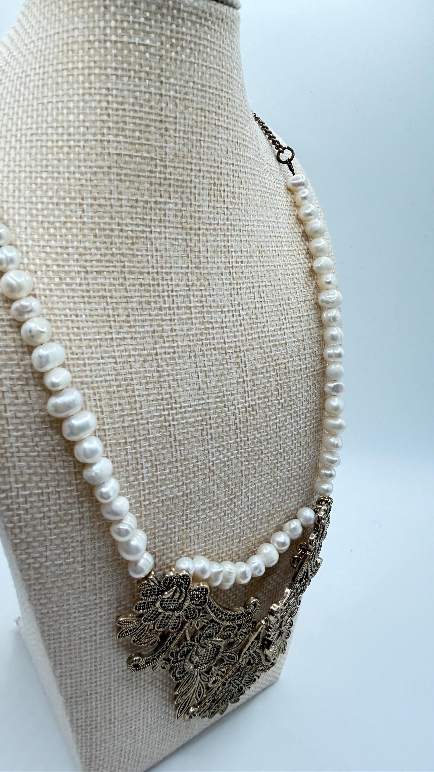 Pearl necklace with an ornate metal pendant on a beige mannequin bust.