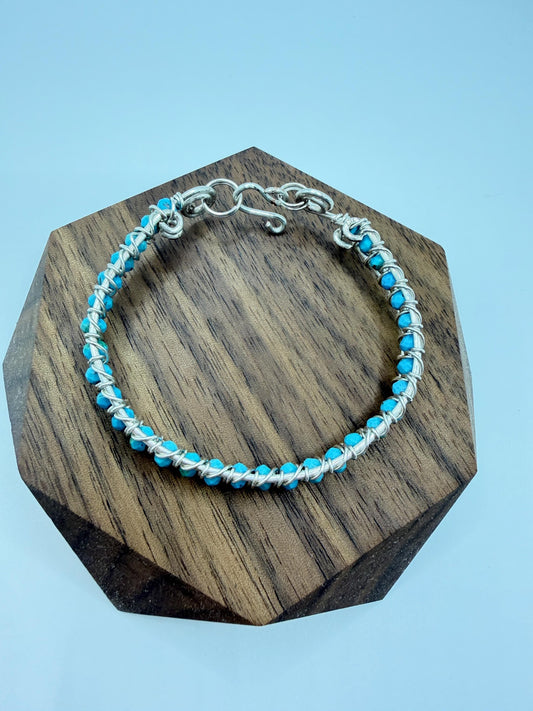 wire wrapped bracelet with blue beads on a wooden hexagonal stand against a light blue background