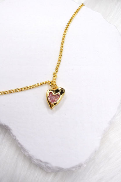 Gold necklace with a heart-shaped pendant on a white background