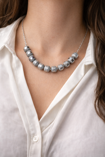 Necklace with gray beads worn by a person in a white shirt