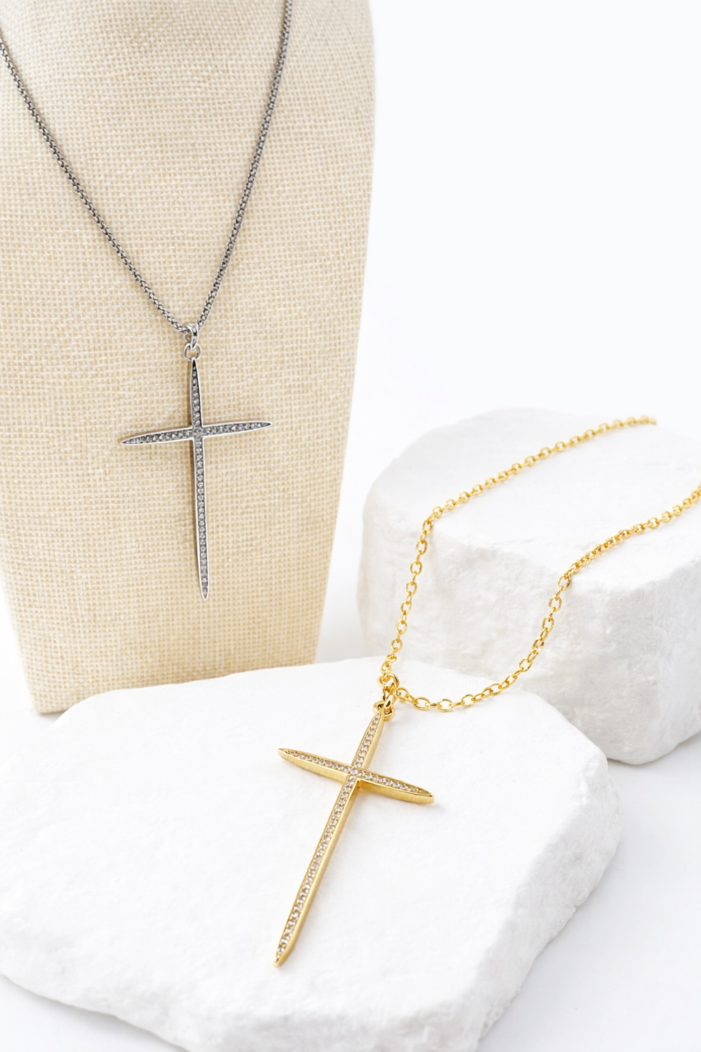 Two cross necklaces, one gold and one silver, on a white surface.