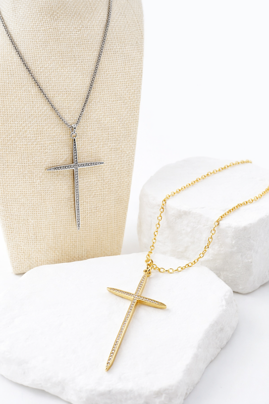 Two cross necklaces, one gold and one silver, on a white surface.