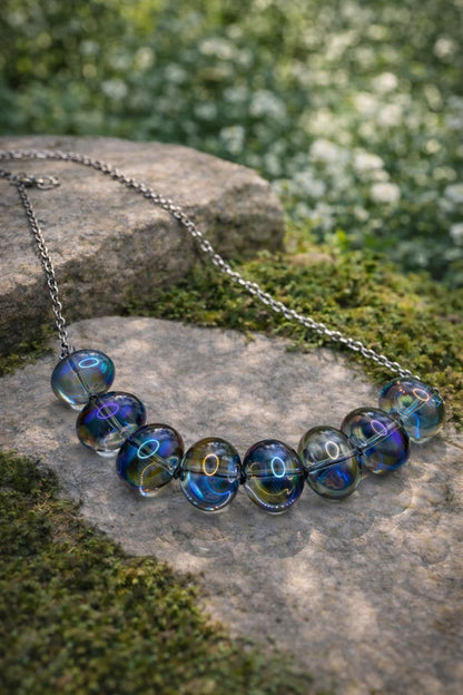 Necklace with blue glass beads on a stone surface with greenery in the background