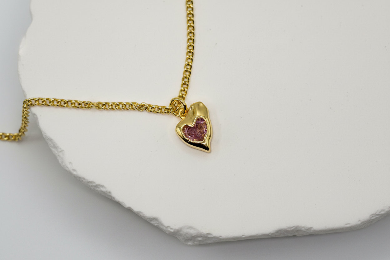 Gold necklace with a heart-shaped pendant on a white background