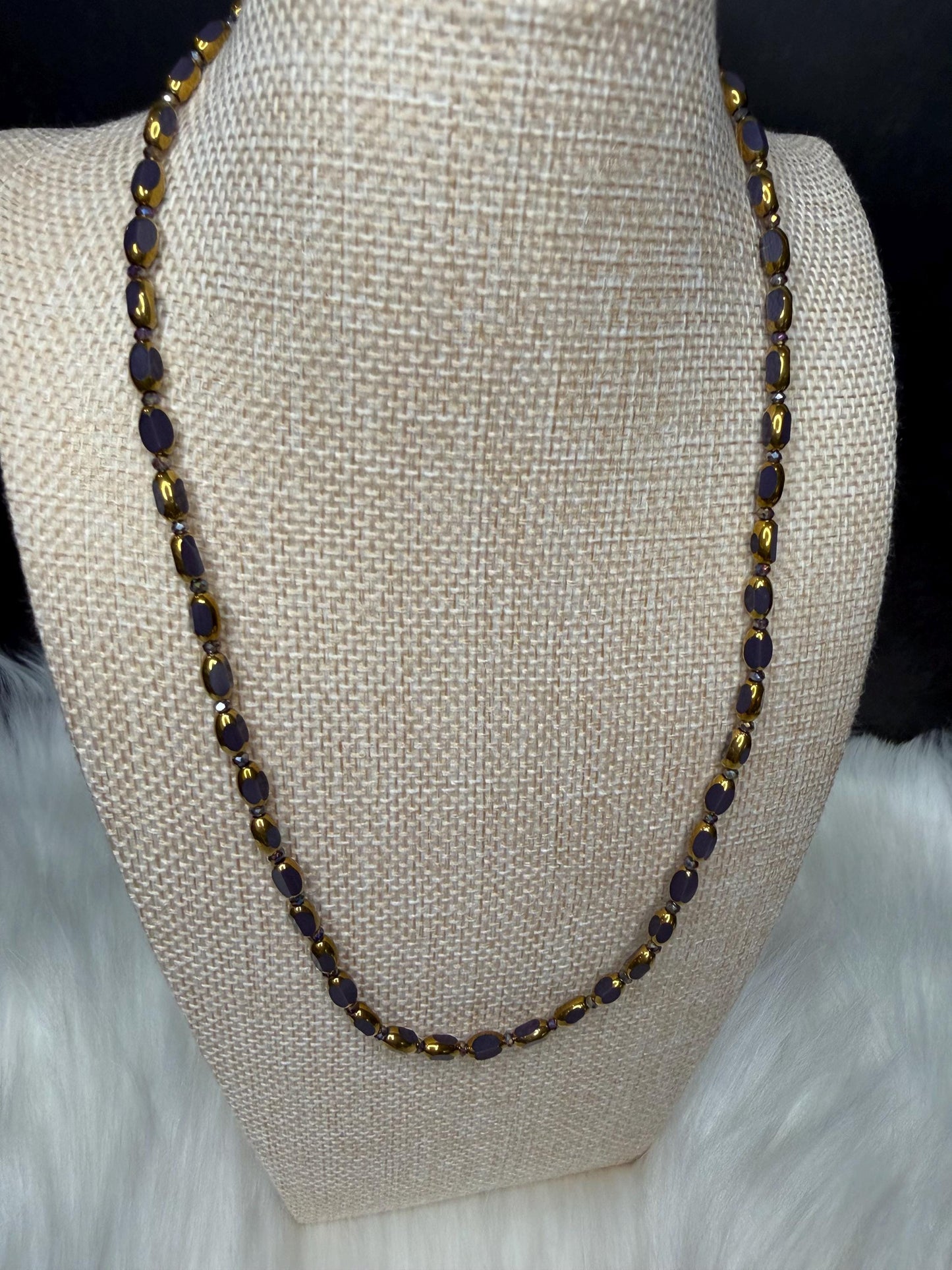 Necklace with purple and gold beads on a mannequin bust.
