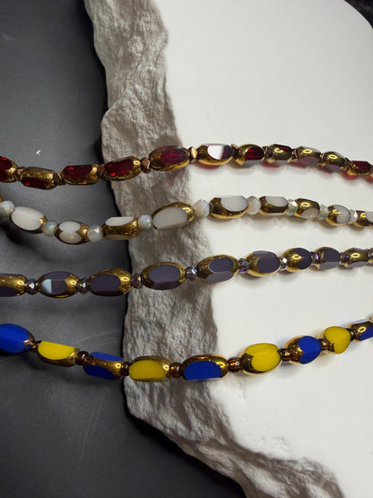 Four beaded necklaces with multicolored beads on a textured surface.