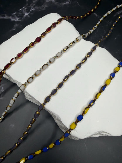 Three beaded necklaces on a white stone surface with a dark background