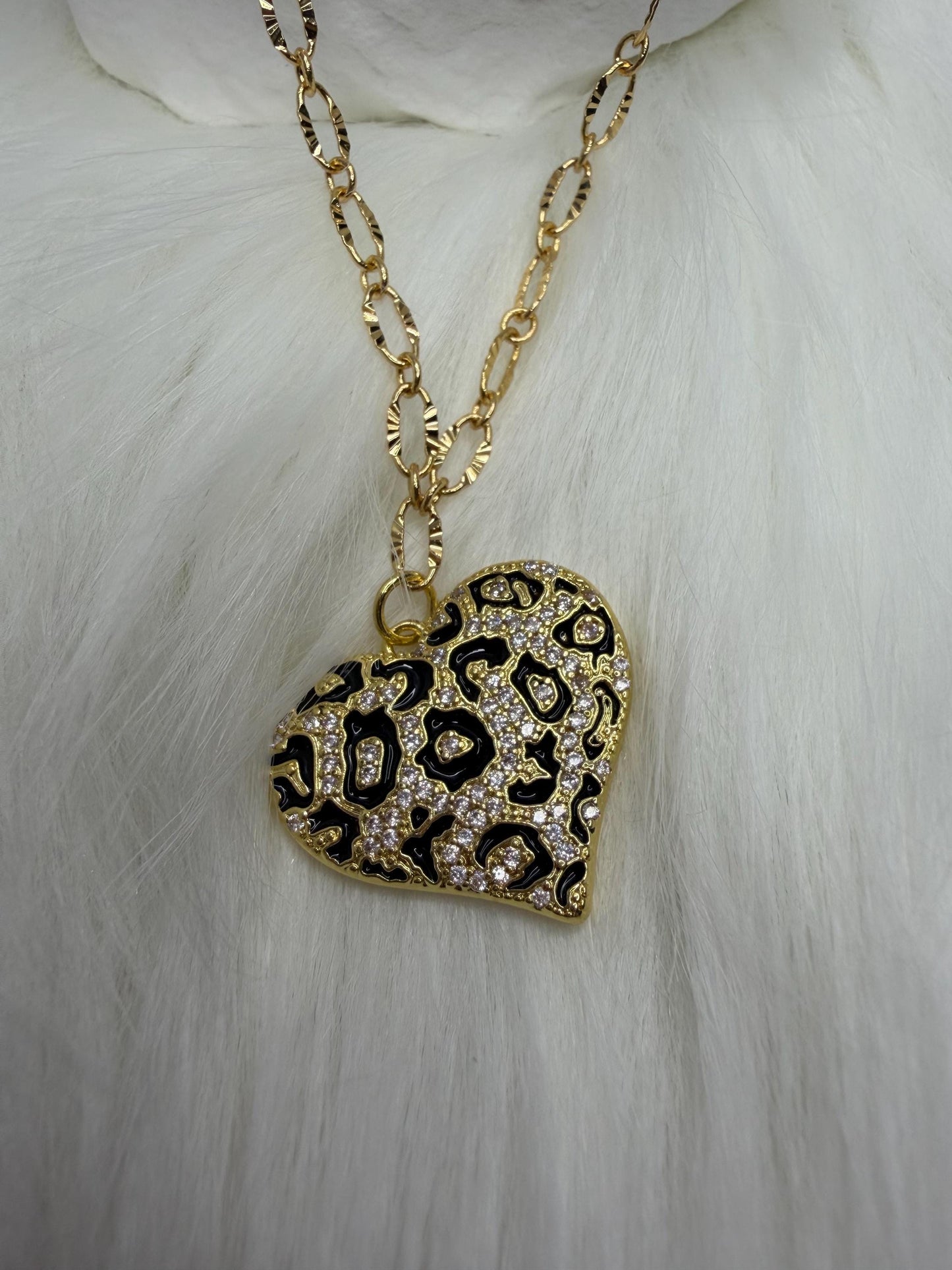 Gold necklace with a leopard print heart pendant on a white fur background