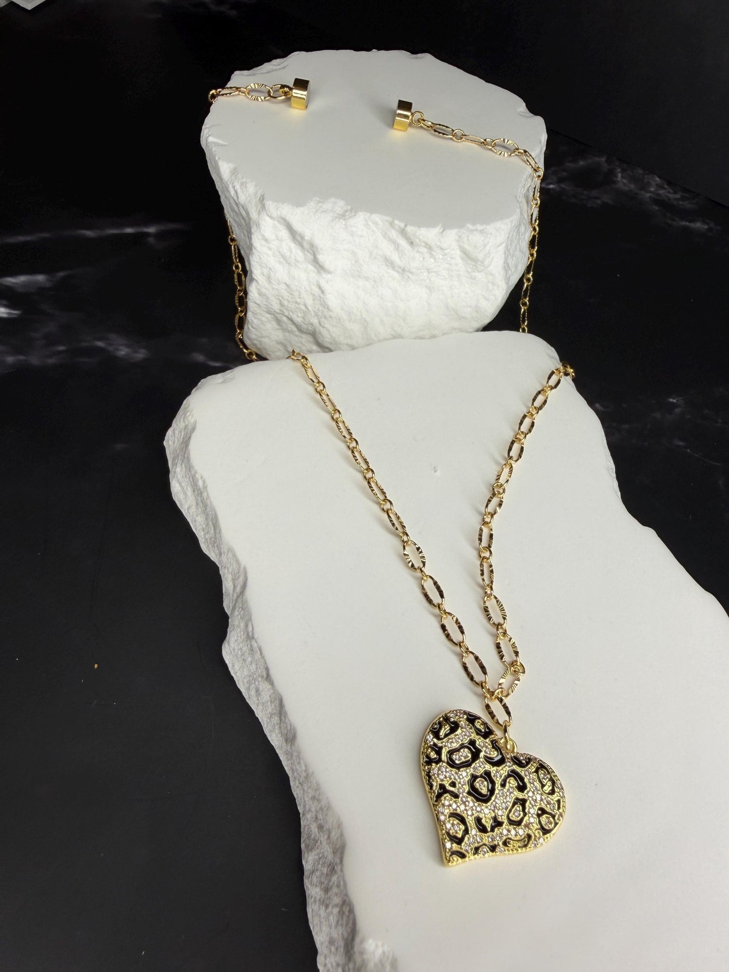 Gold necklace with a heart-shaped pendant on a white stone surface