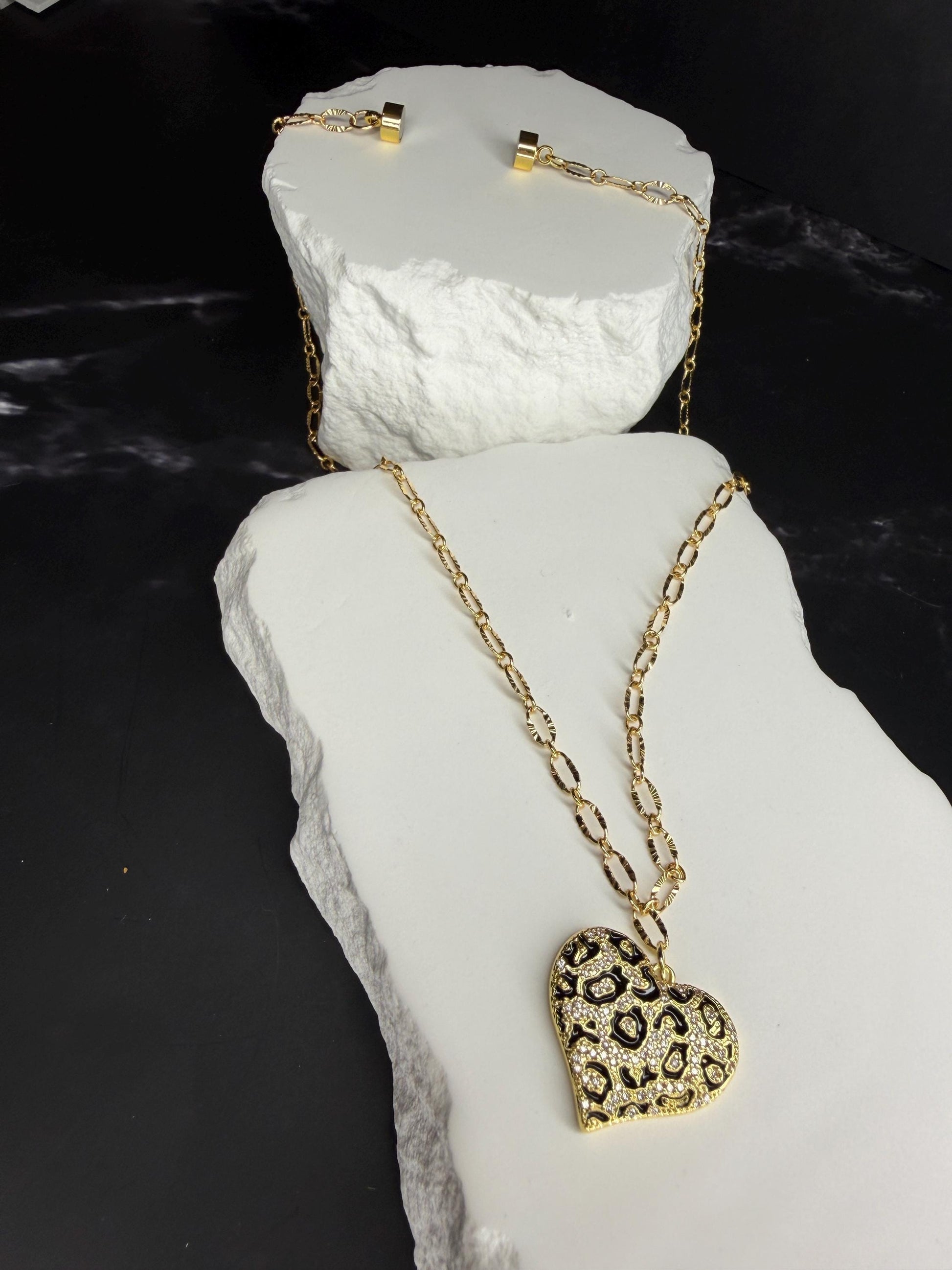 Gold necklace with a heart-shaped pendant on a white stone surface