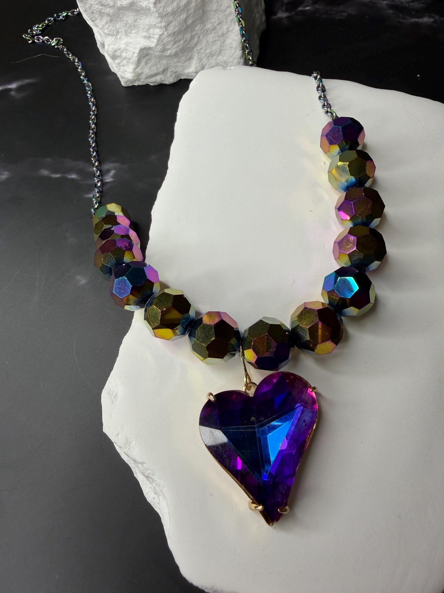 Necklace with multicolored beads and a heart-shaped purple pendant on a white stone surface.