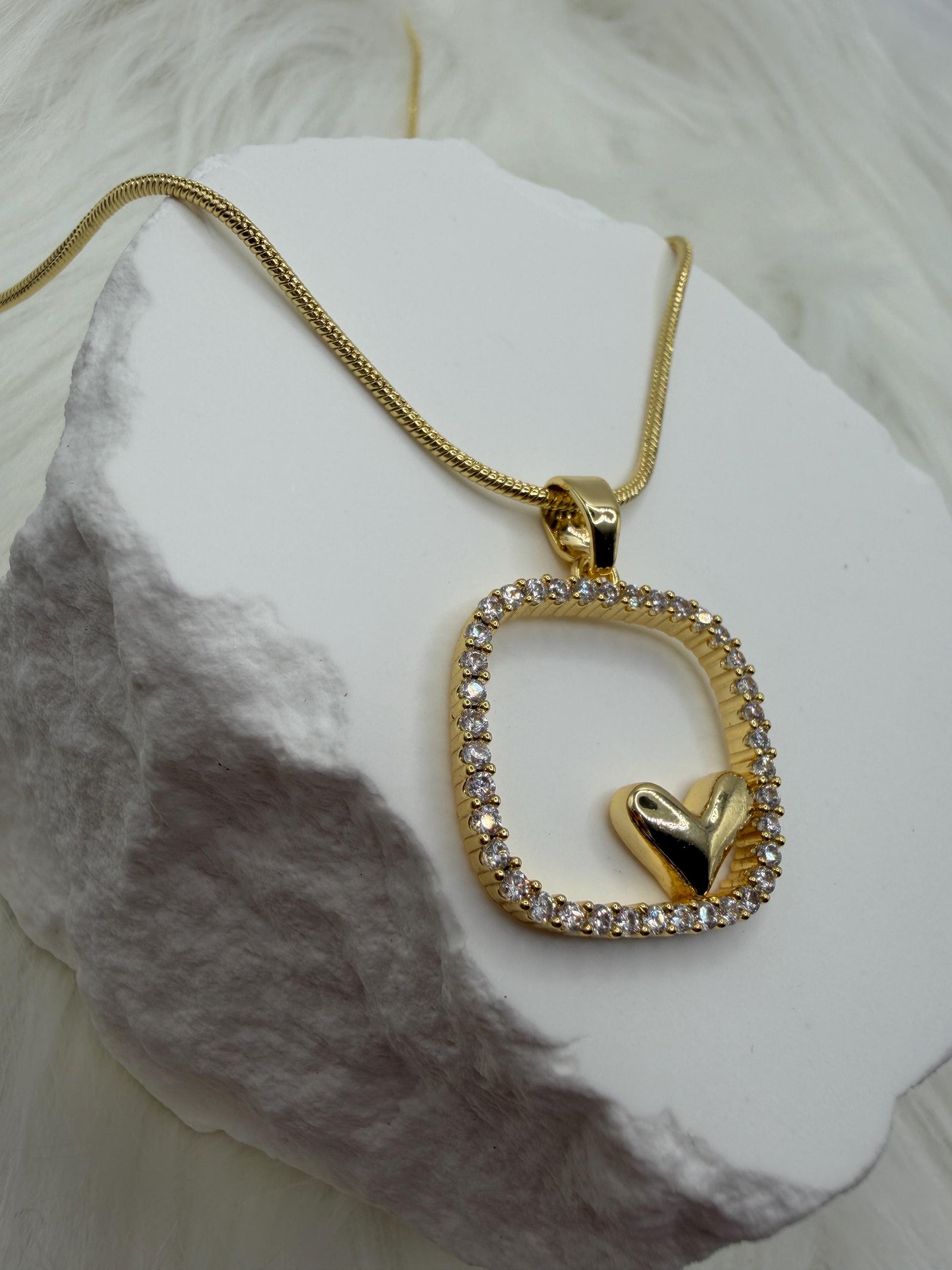 Gold necklace with a heart-shaped pendant on a white stone surface