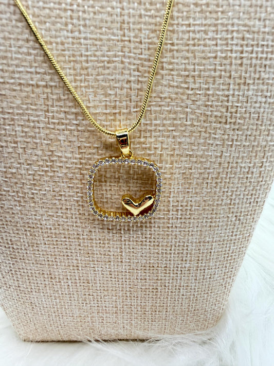 Gold necklace with a heart-shaped pendant on a textured beige surface