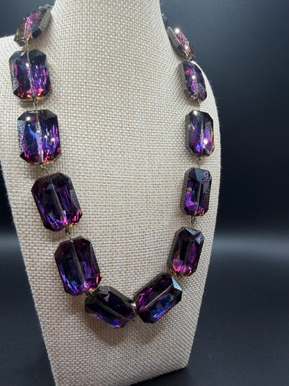 Necklace with purple crystals on a gray stand against a dark background
