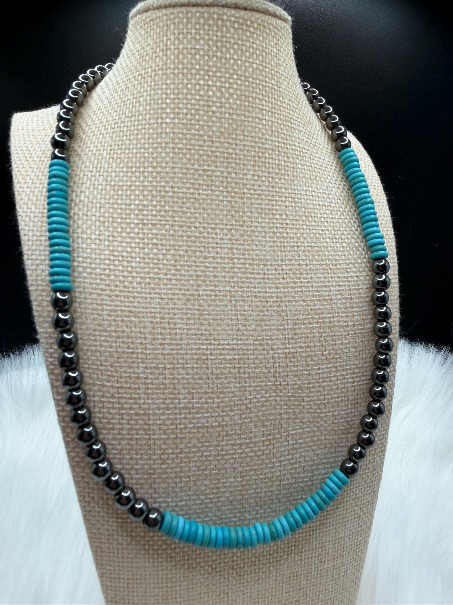 Necklace with turquoise and hematite beads on a beige bust