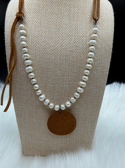 Pearl necklace with a brown leather cord and pendant on a beige fabric stand.