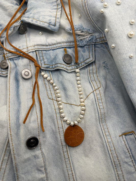 Pearl necklace with a leather pendant draped over a denim jacket.