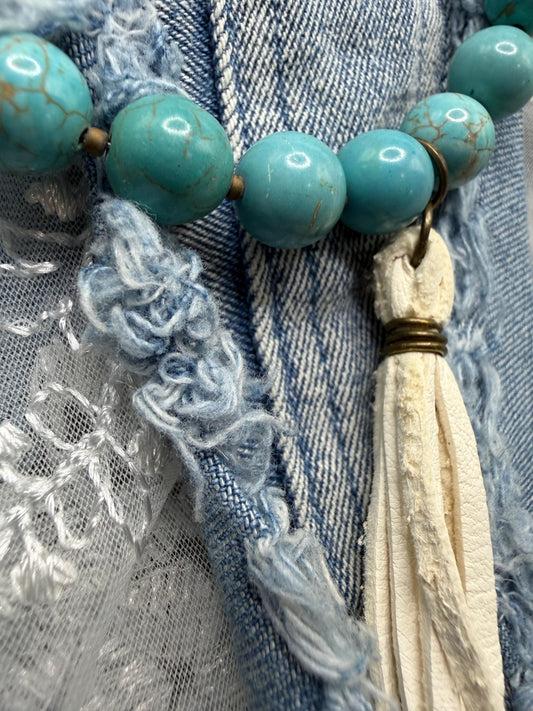 Necklace with turquoise beads and tassel on a textured fabric background