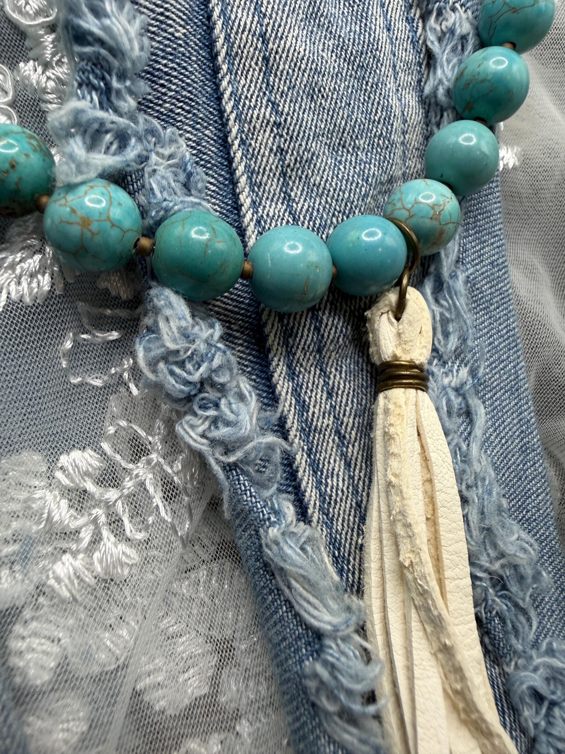 Turquoise beaded necklace with tassel on a textured fabric background