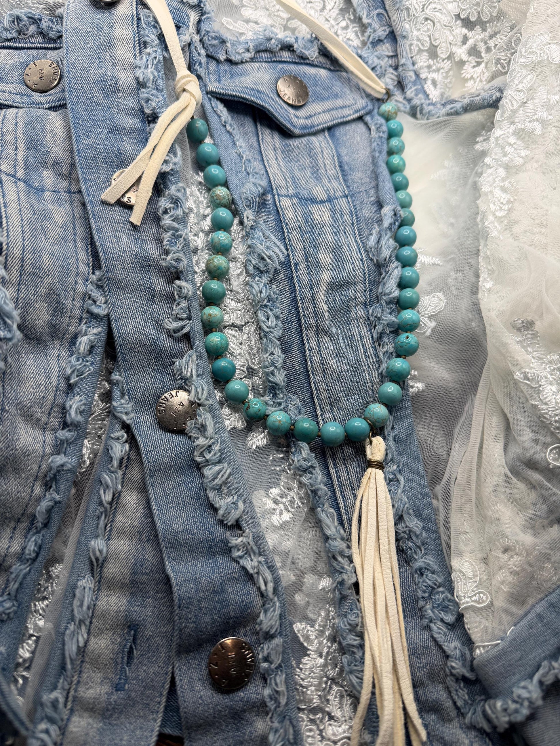Close-up of a blue denim jacket with a turquoise beaded necklace and tassels.