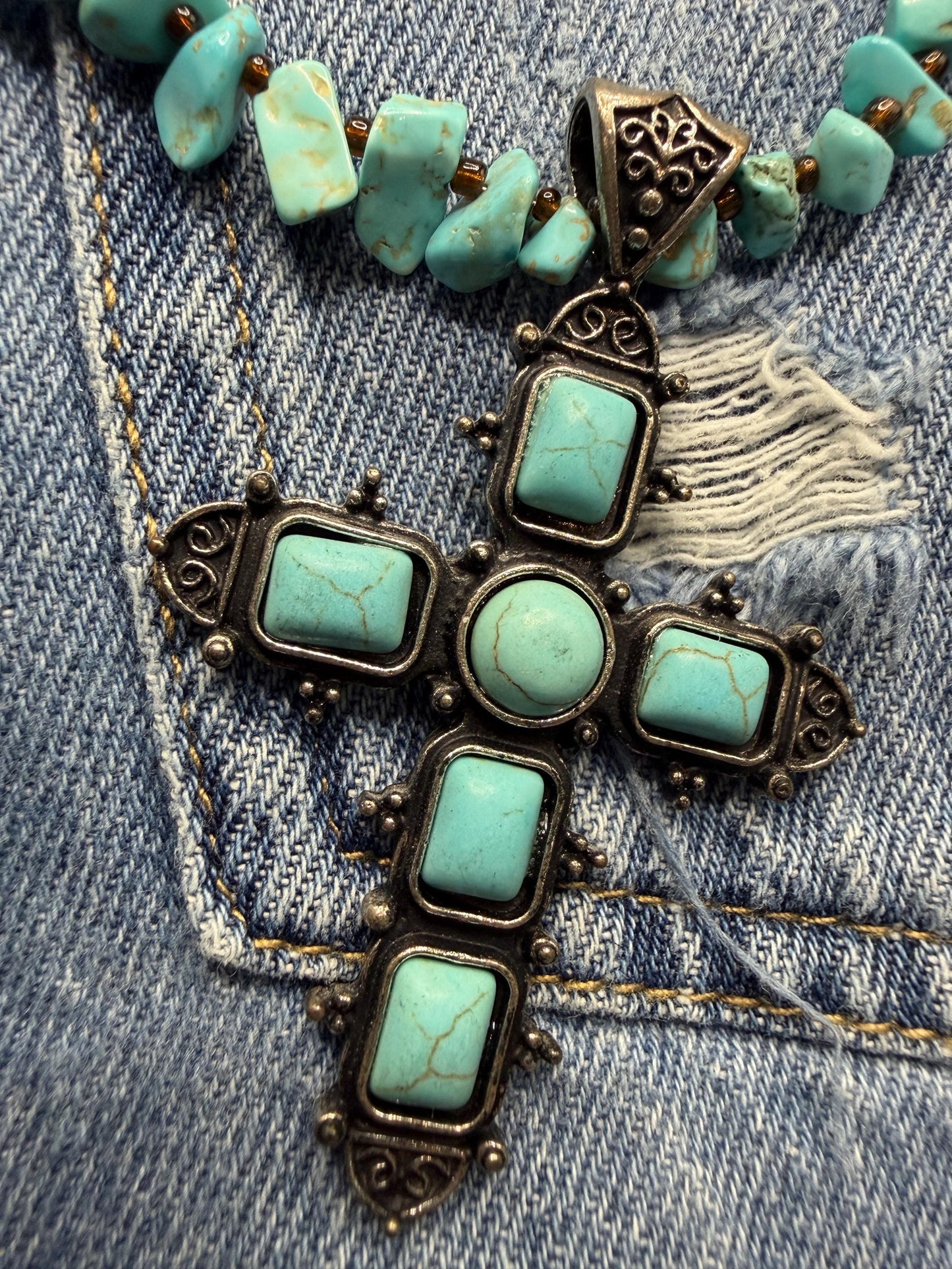 Necklace with turquoise stones and bronze cross pendant on denim fabric