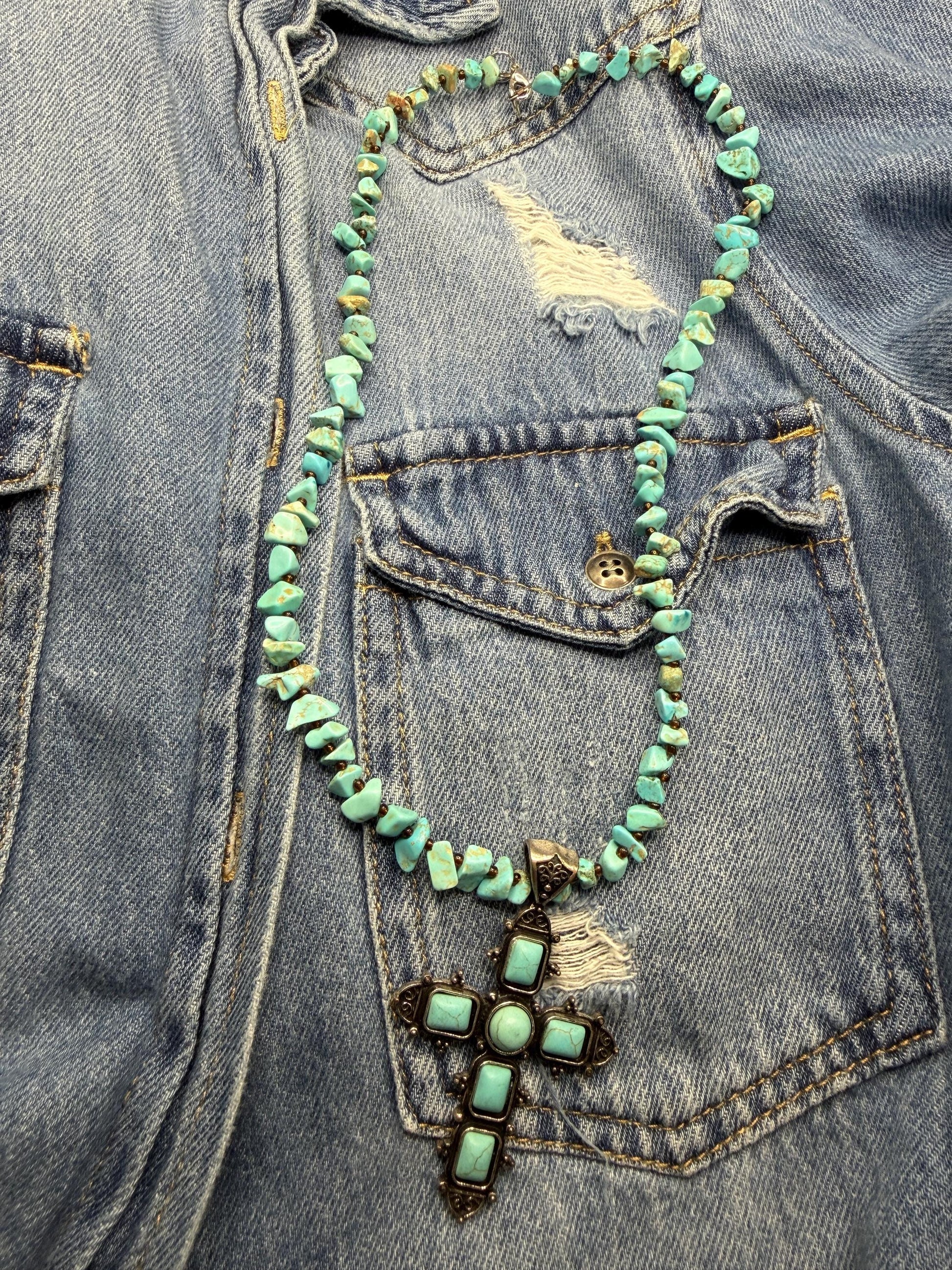 Turquoise beaded necklace with a cross pendant on a denim jacket.