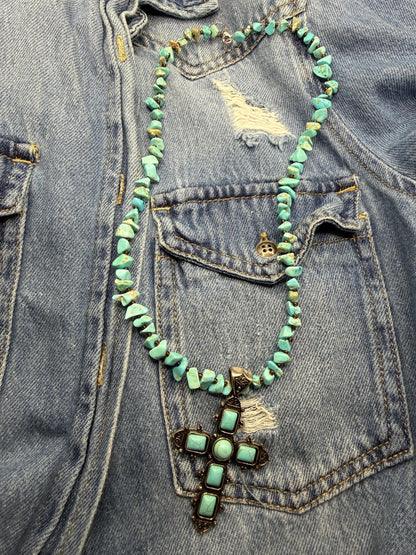 Turquoise beaded necklace with a cross pendant on a denim jacket.