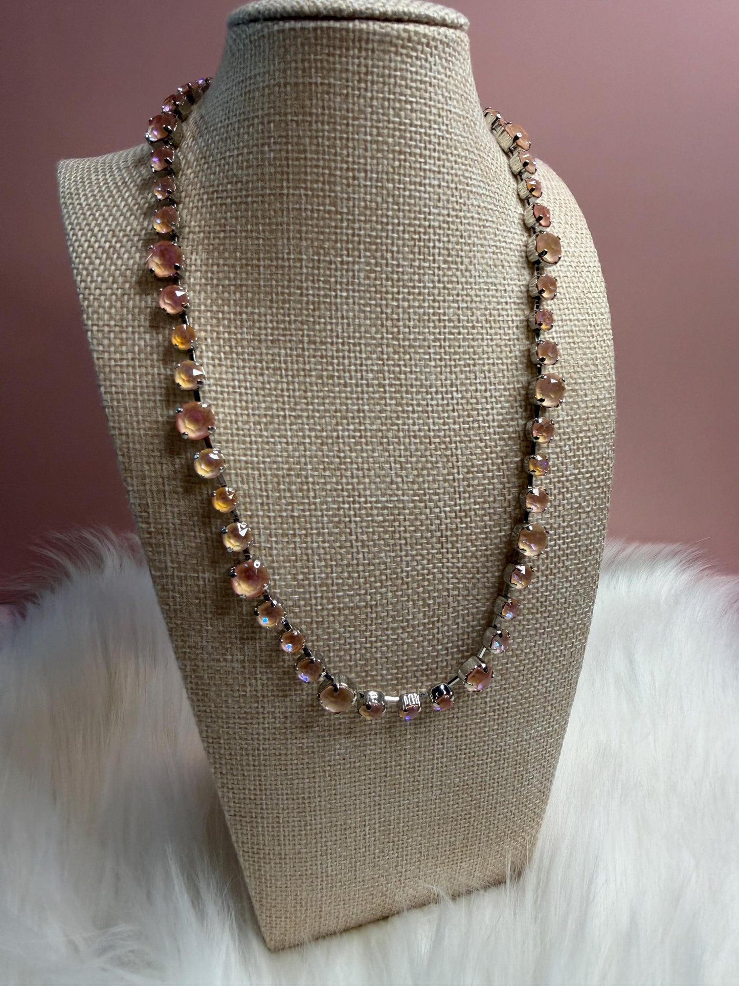 Necklace with aurora crystals  on a beige bust against a soft pink background