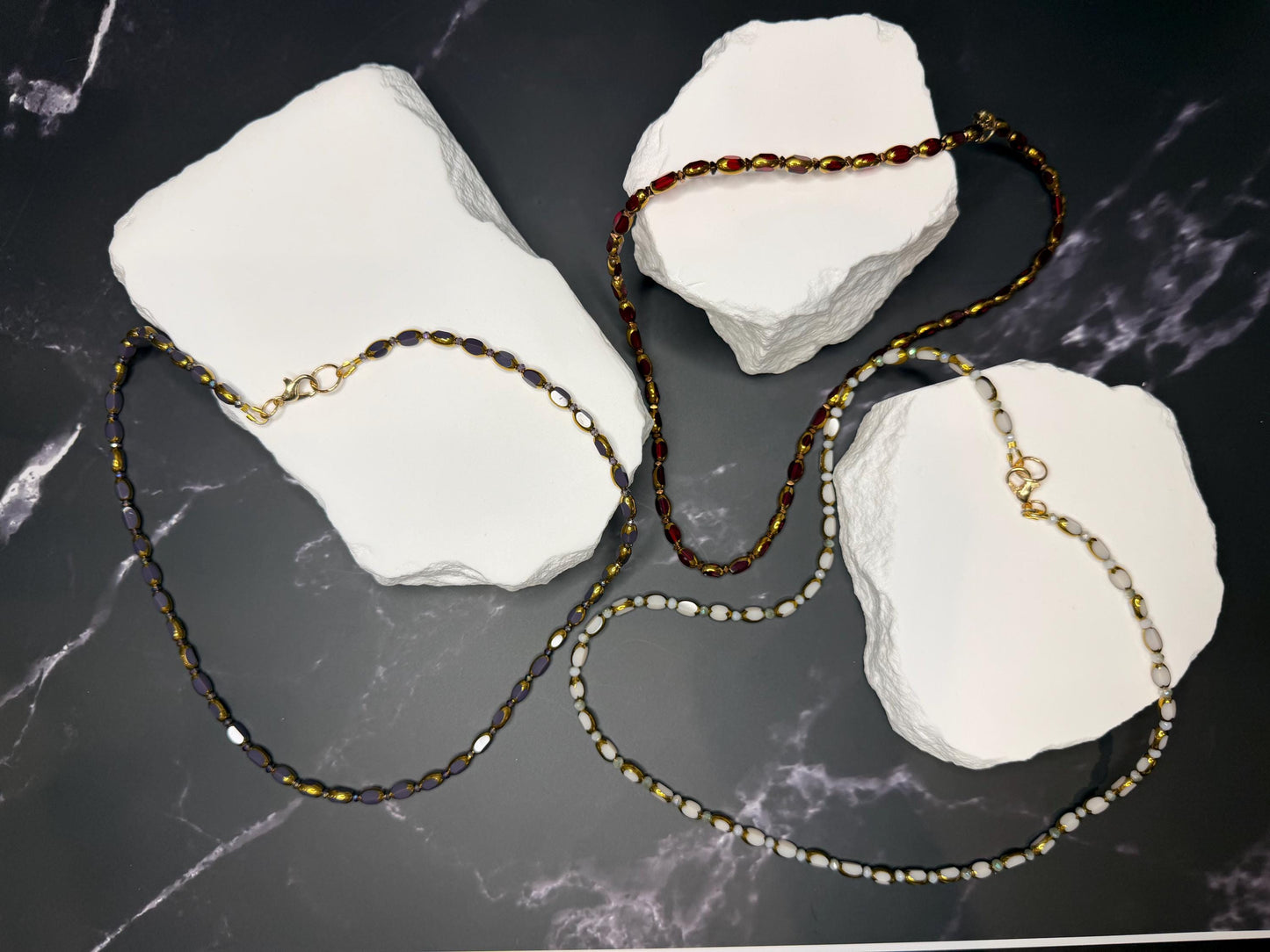 Three necklaces on white stones with a dark marble background