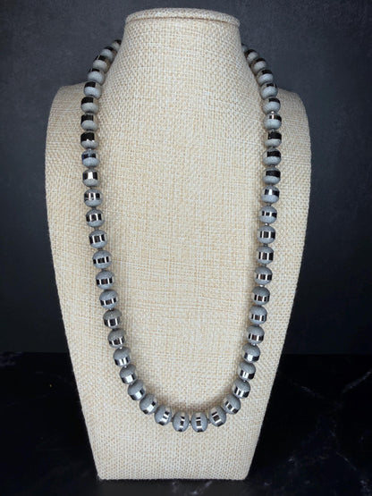 Necklace with gray beads on a beige bust against a dark background