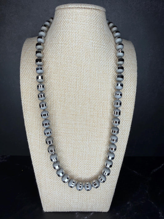 Necklace with gray beads on a beige bust against a dark background