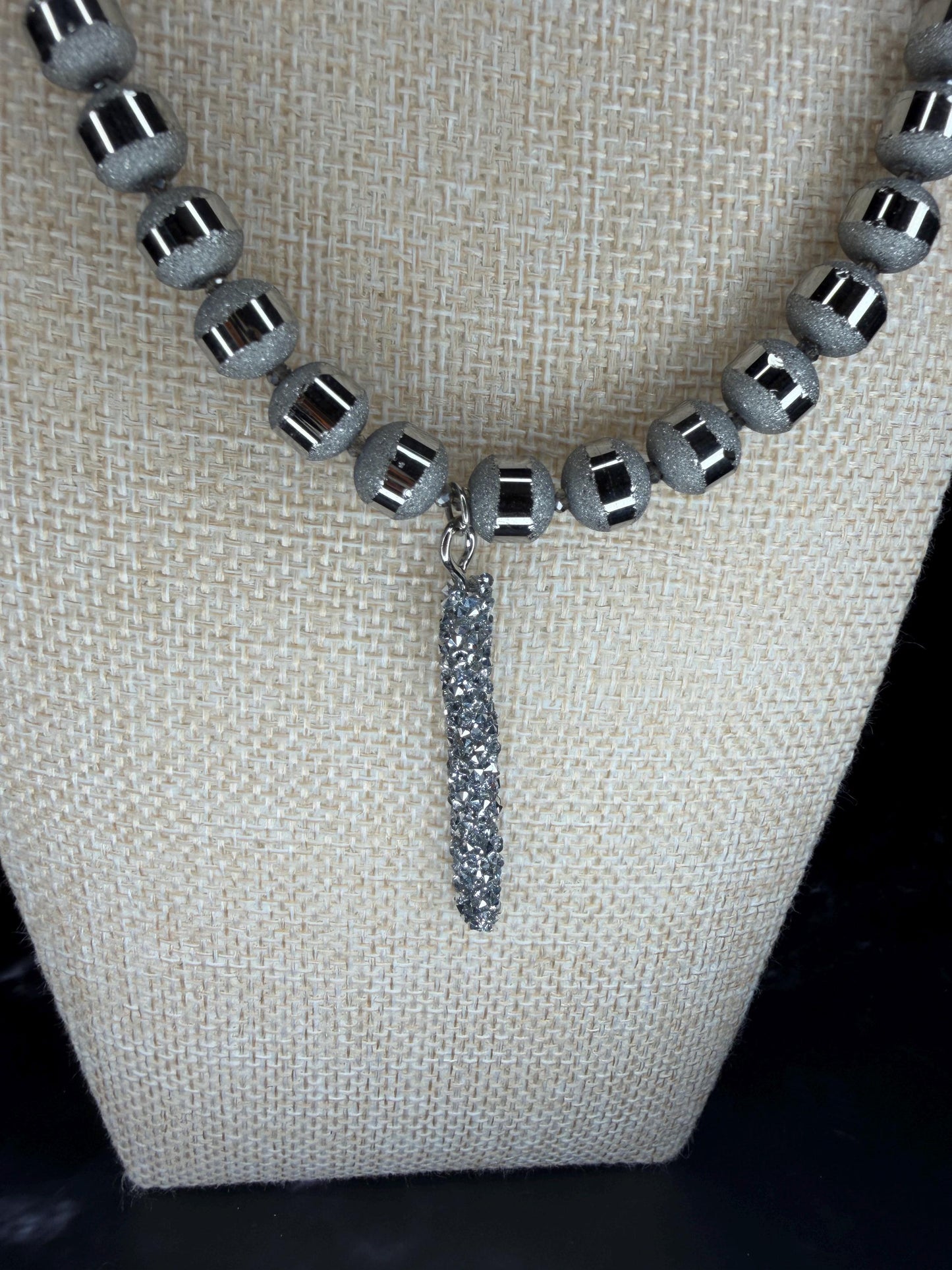 Necklace with gray beads and a dangling silver pendant on a beige fabric background