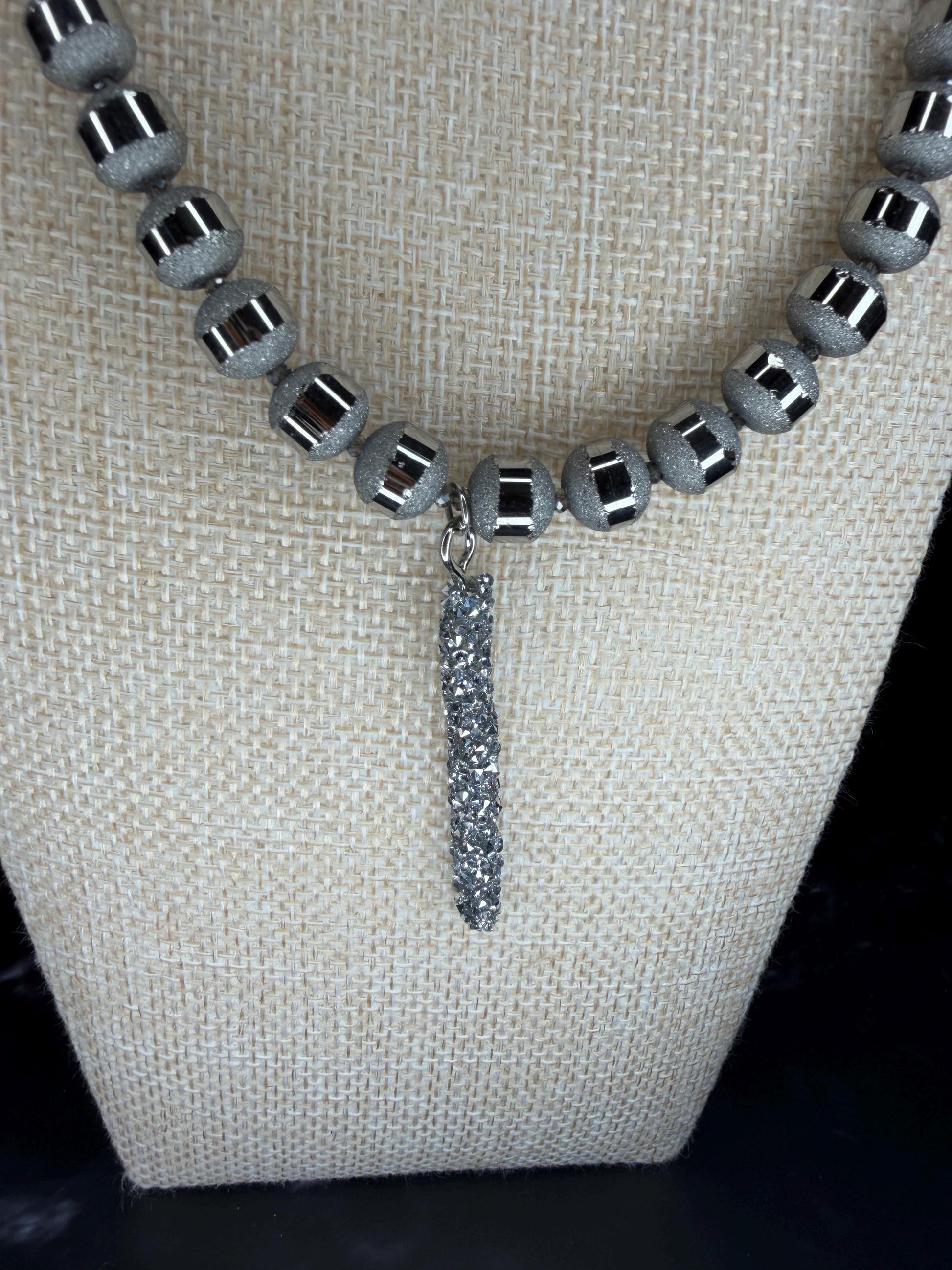 Necklace with gray beads and a dangling silver pendant on a beige fabric background