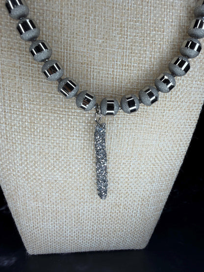 Necklace with gray beads and a dangling silver pendant on a beige fabric background