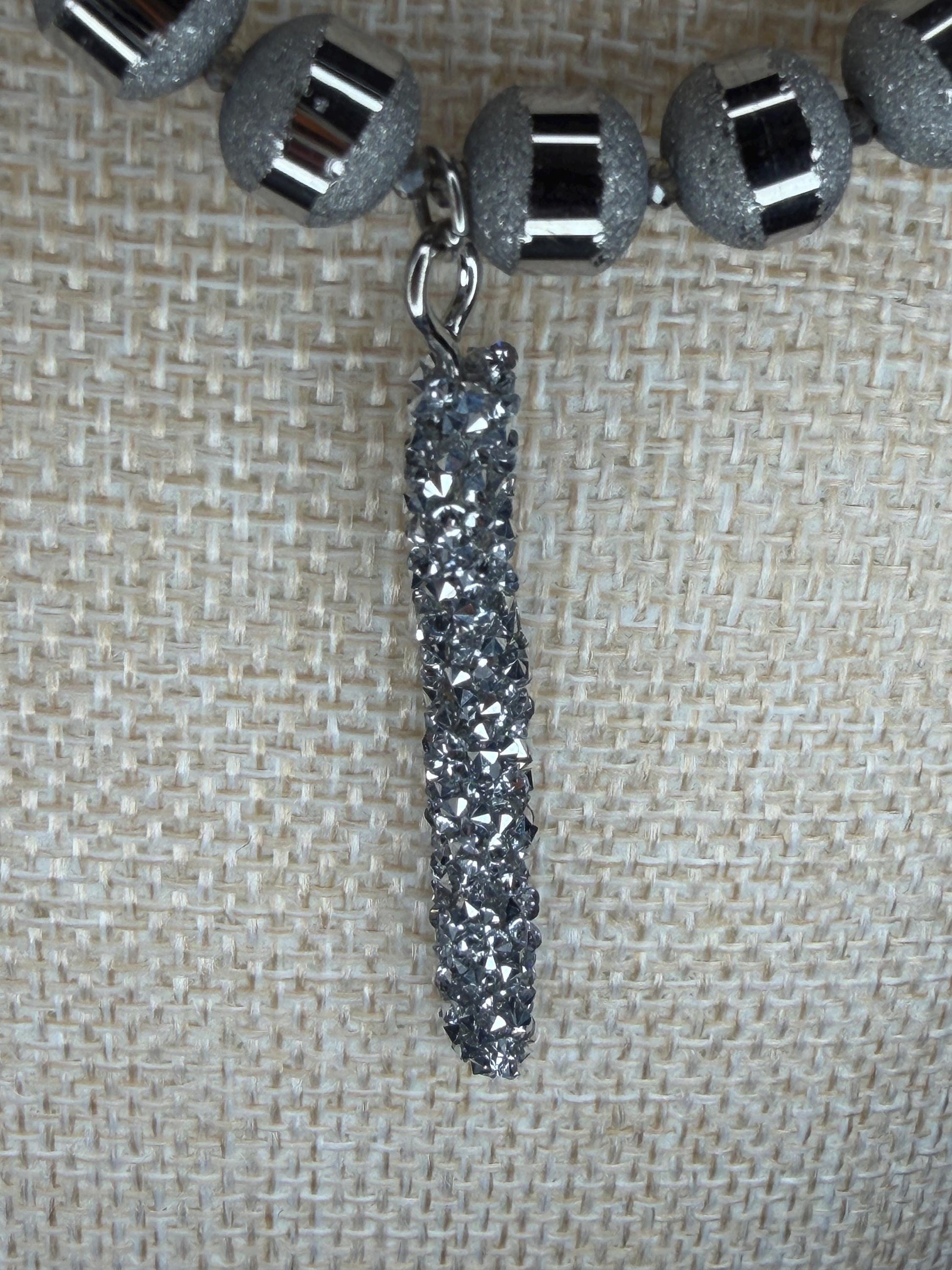 Close-up of a necklace with silver sparkly beads and a silver pendant on a textured beige background