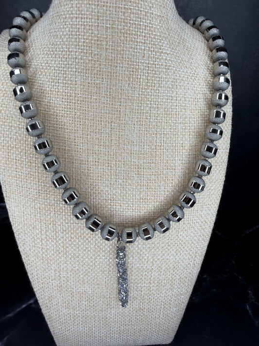 Necklace with square beads and a dangling crystal on a mannequin bust.