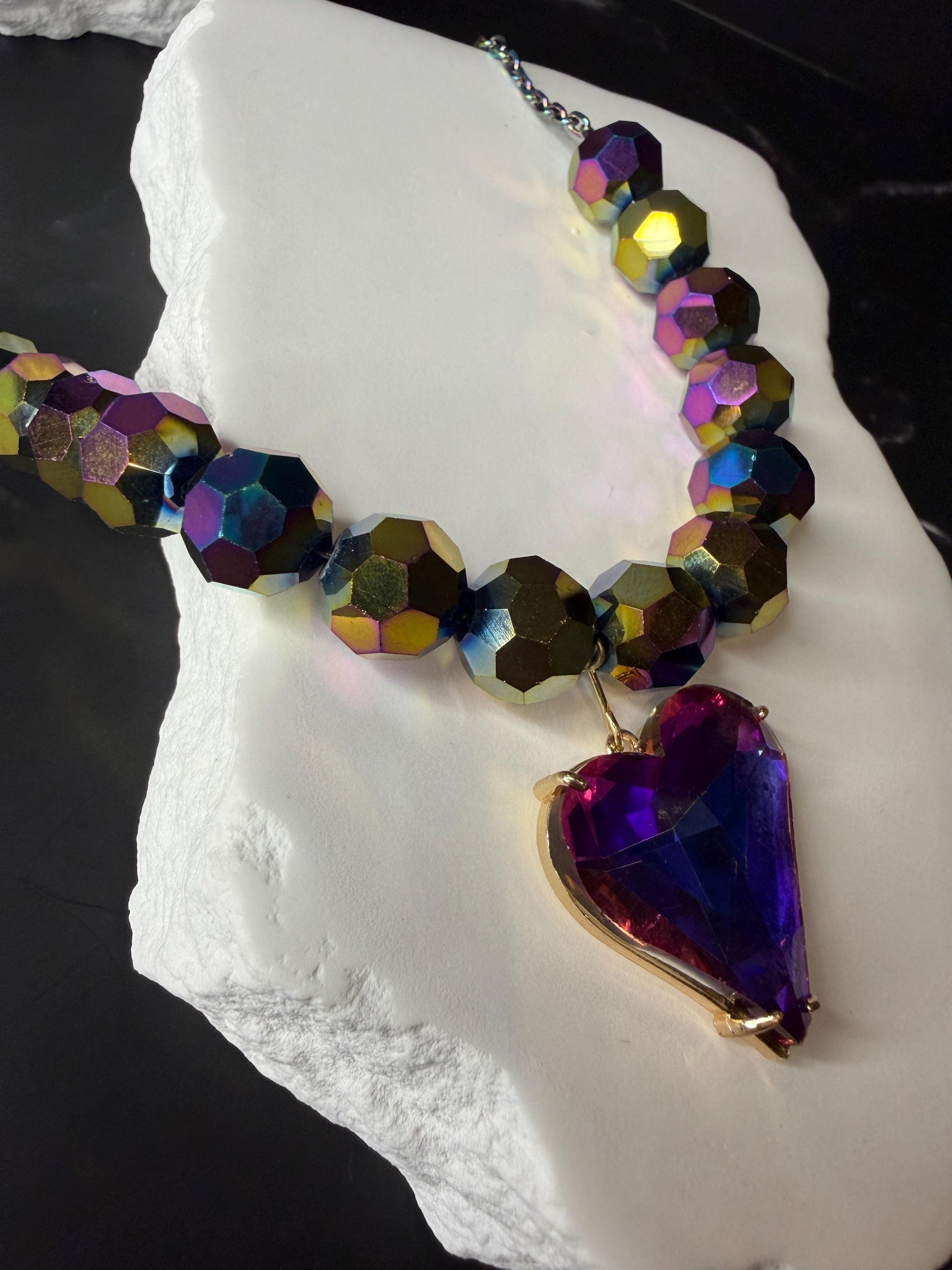 Necklace with multicolored beads and a heart-shaped purple pendant on a white stone surface.