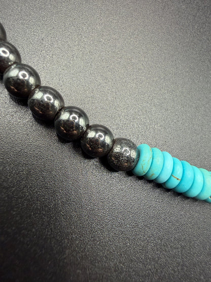 Necklace with hematite beads and turquoise accents on a dark surface