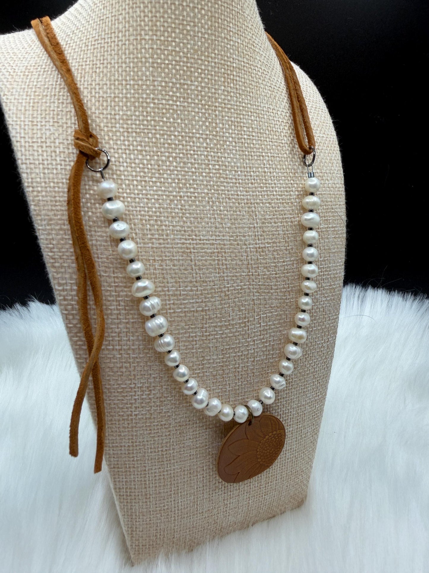 Pearl necklace with a brown leather strap on a mannequin bust.