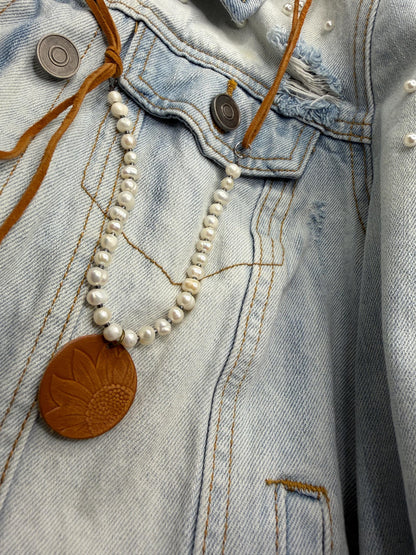 Close-up of a necklace with a brown leather pendant on a denim jacket.