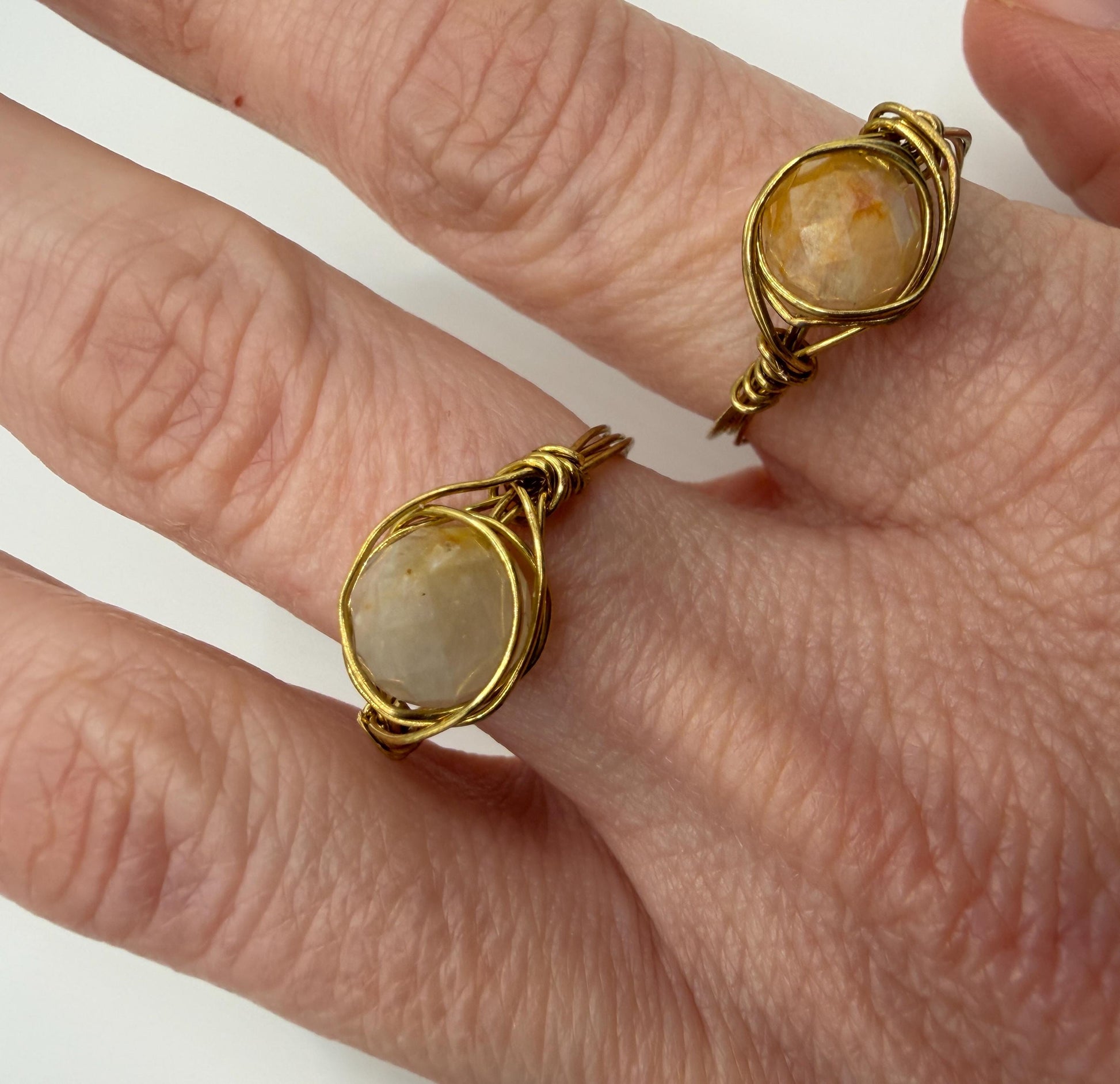 Gold rings with stone inlays on a person's fingers against a white background