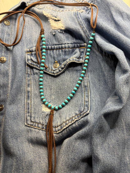 Turquoise beaded necklace with tassel hanging from a denim jacket.