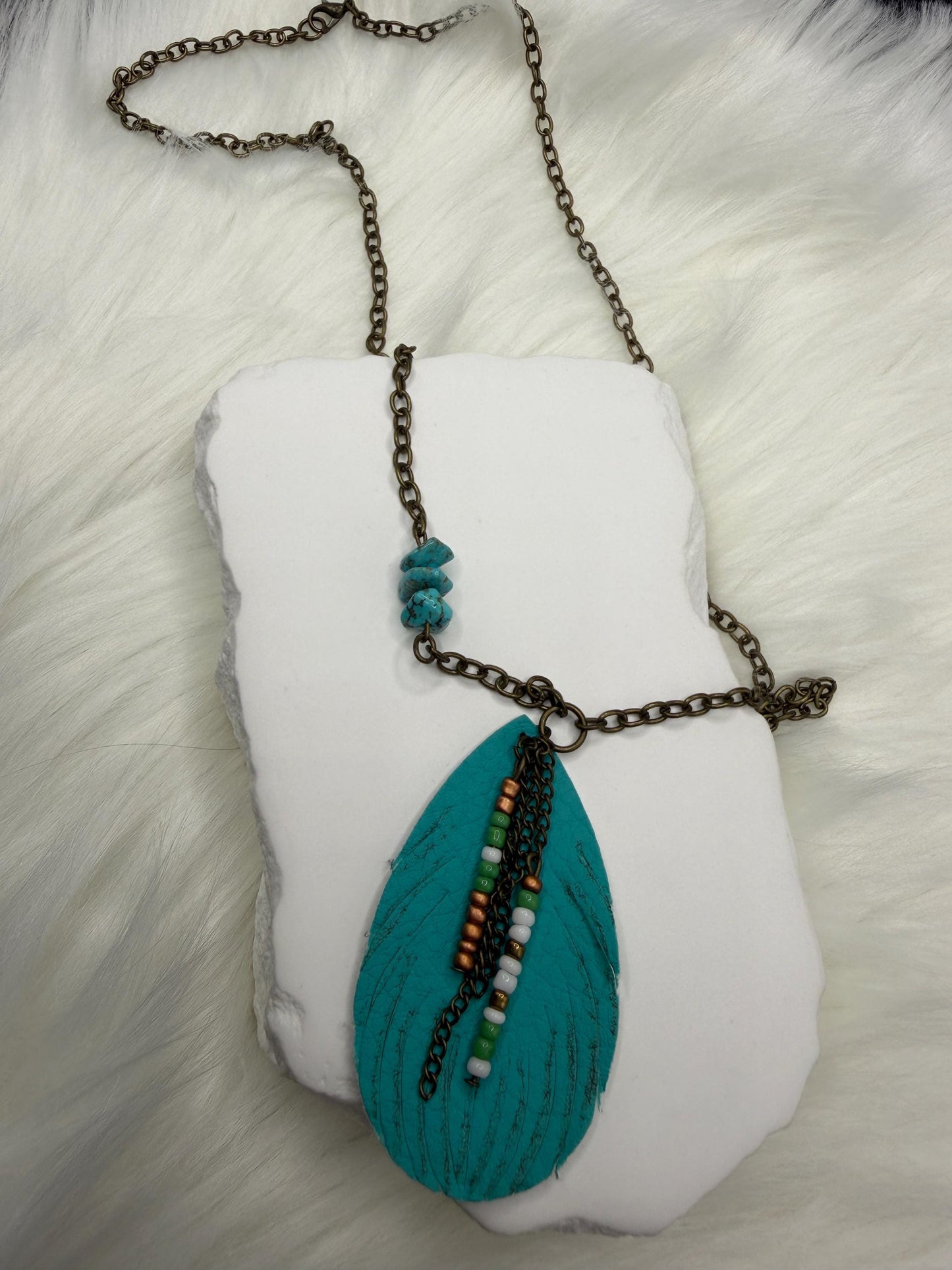 Necklace with a large turquoise leaf pendant on a white cushion