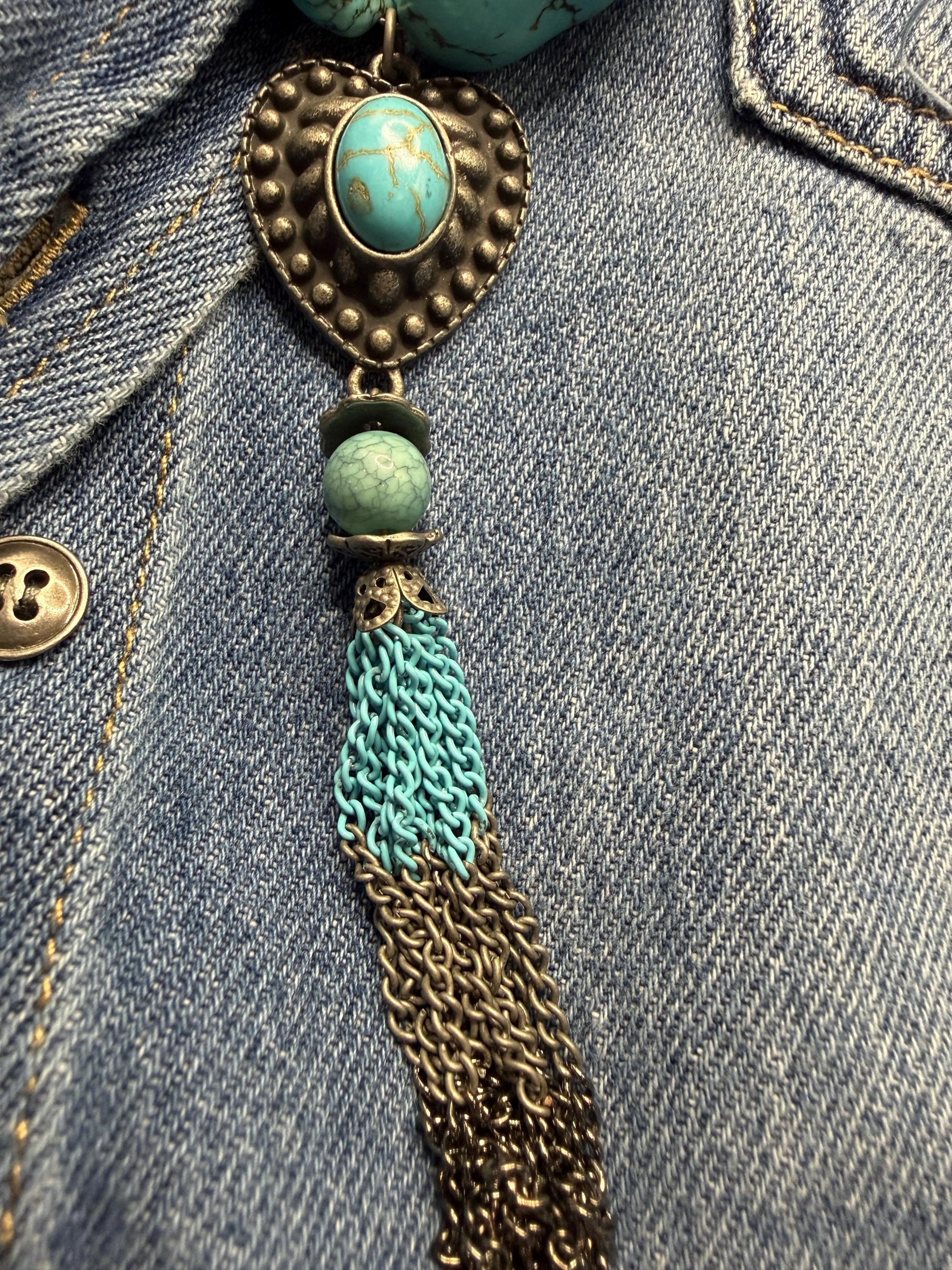 Decorative pendant with turquoise stones and tassel on a denim background