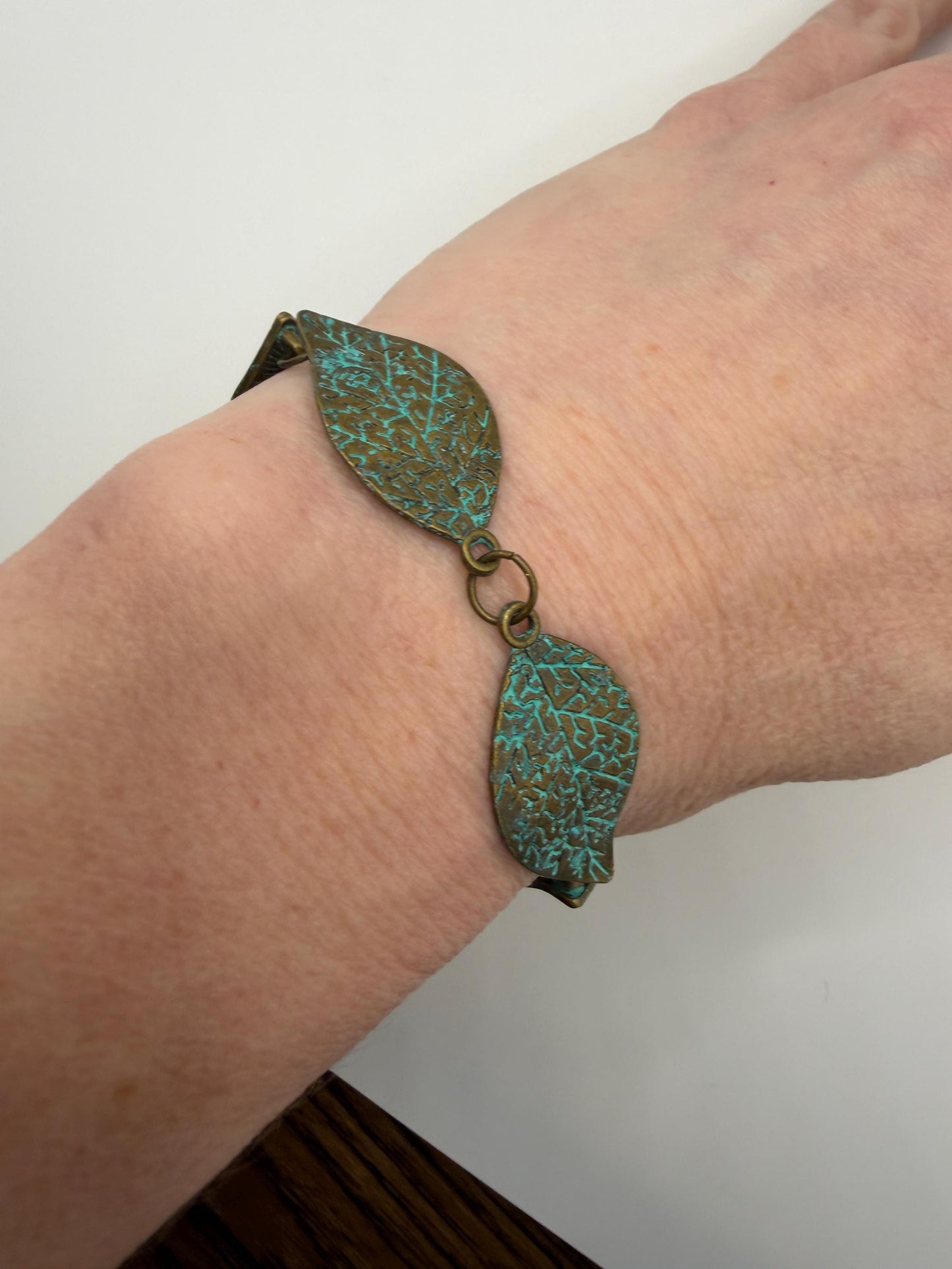 Bracelet with leaf-shaped turquoise stones on a wrist against a neutral background